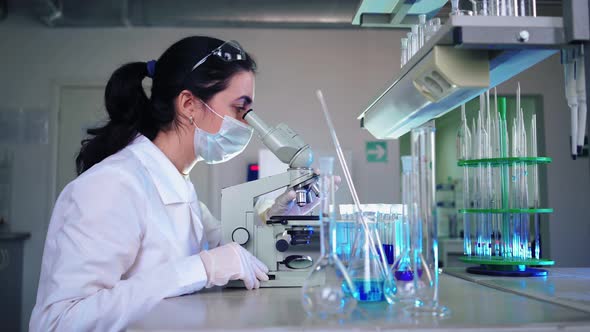 Female Microbiologist Looking Into Microscope in Medical Science Laboratory