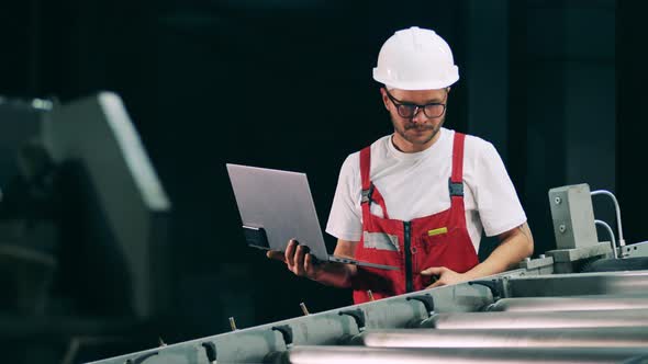 Metallurgy Worker with a Laptop Is Observing a Working Conveyor