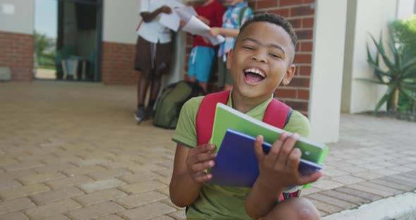 Video of happy african american boy holding books in front of school