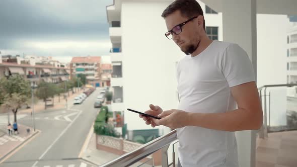 Handsome Man Is Standing on a Terrace of Flat and Reading Sms on Phone