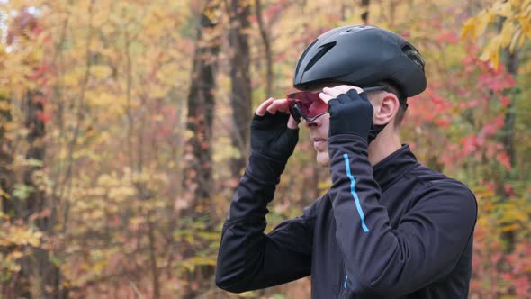 Professional male cyclist in black sports apparel and helmet preparing for training in autumn park