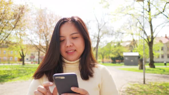 Asian woman with black straight hair and happy face. Walking and using her smartphone