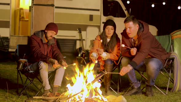 Friends Relaxing Around Camp Fire and Roasting Marshmallows on Sticks