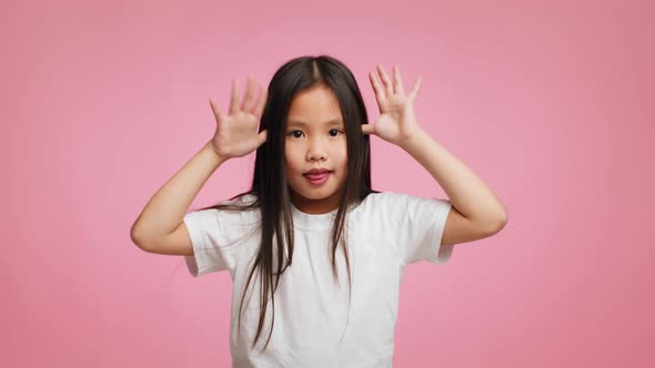 Asian Kid Girl Grimacing Holding Hands Near Temples Pink Background