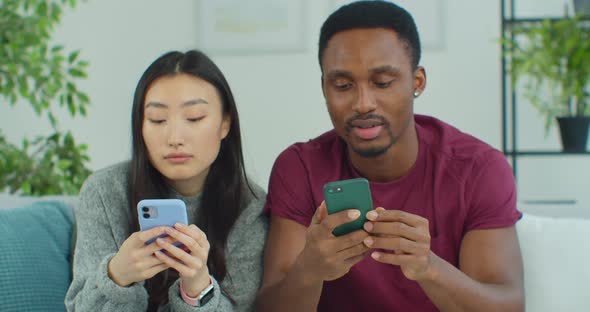 Young Mixed Ethnicity Couple Using Smartphone While Sitting on Sofa at Home