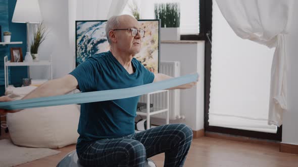 Elder Man Pulling Resistance Band to Stretch Muscles at Home
