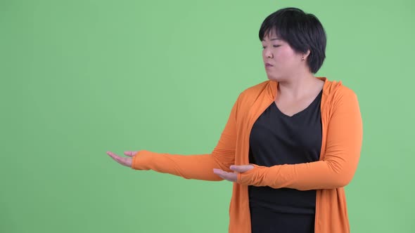 Stressed Young Overweight Asian Woman Showing Something Ready for Gym