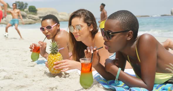 Side view of mixed-race female friends drinking cocktail drinks on the beach 4k