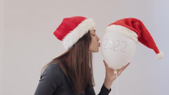 Young Female Green Shirt and Red Santa Hat Holding White Balloon Kissing It