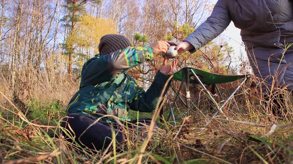 Mom Gives Her Son a Mug of Hot Tea Sitting in the Grass