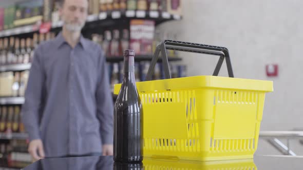 Adult Caucasian Man Coming To the Counter in Liquor Shop, Putting Bottle of Red Wine Into Yellow