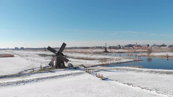 Ice skaters on frozen canal beside Netherlands windmill, winter aerial view