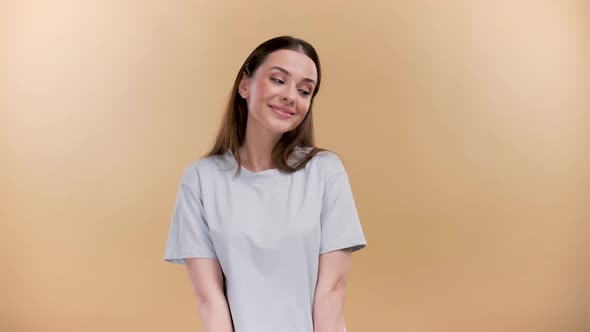 Playful Shy Young Caucasian Woman Hiding Face Looking Down and Flirting with a Camera on a Beige