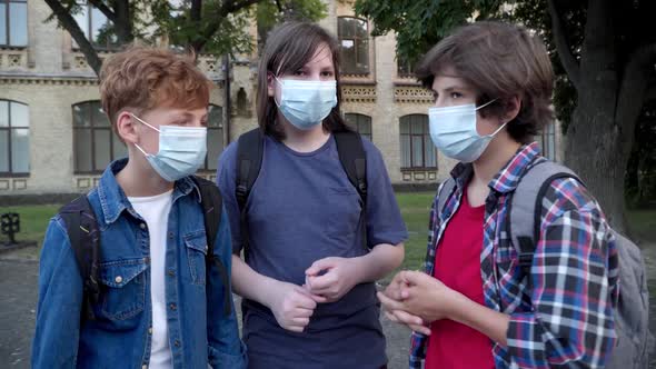 Three Caucasian Schoolboys in Covid Face Masks Talking After Learning on Schoolyard. Classmates