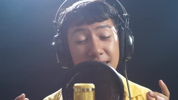 Young Asian Boy With Headphone Singing Into A Condenser Microphone On The Black Background