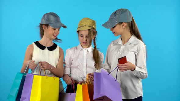 Girls Show Off Bags in Each Other’s Hands. Blue Background
