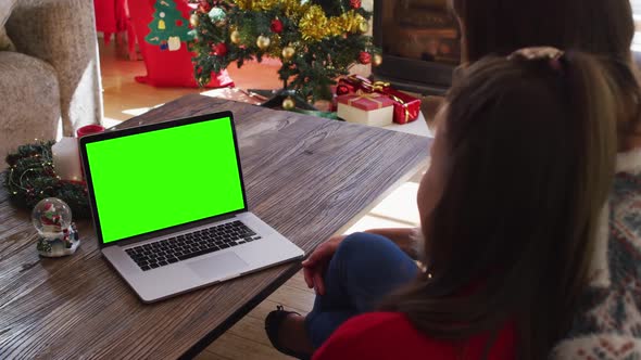 Caucasian mother and daughter waving looking at laptop with green screen sitting on the couch at hom