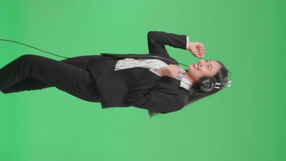 Side View Of Asian Business Woman Listening To Music With Headphones And Dancing On Green Screen