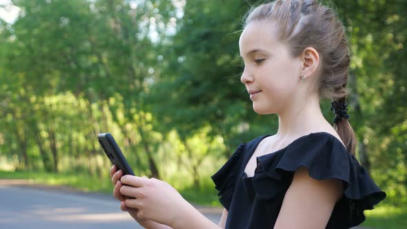 Schoolgirl Looks at Phone and Shows Thumbup Smiling in Park