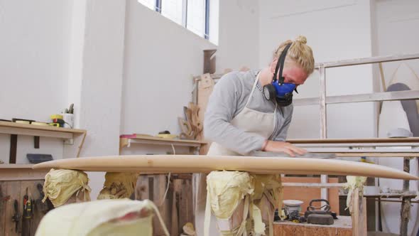 Caucasian male surfboard maker wearing a face mask and polishing a surfboard