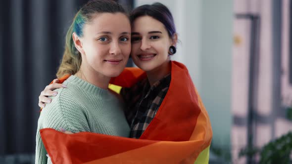 Cheerful Women Wrapped in Colorful Rainbow Flag at Home