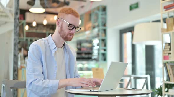 Redhead Man with Laptop Looking at Camera in Cafe