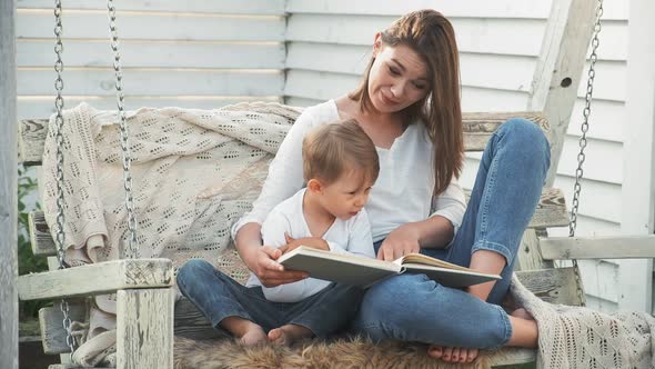 Mother and Child Reading Book Sitting on Swing in the Backyard