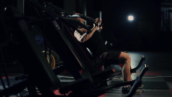 A Muscular Man Performs Exercises on Pectoral Muscles in a Dark Gym, Lifting Weights