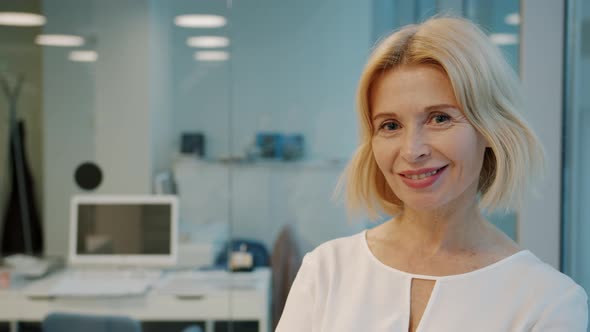 Slow Motion Portrait of Mature Blonde Employee Smiling in Glass Wall Office