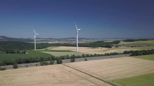 Aerial orbit of windmills turbines in farm fields at daytime generating clean renewable energy for s