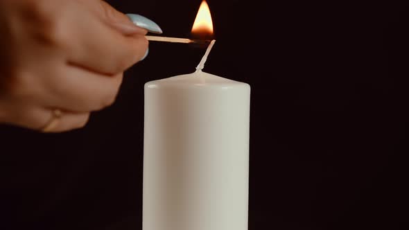 A Woman's Hand Lights a Wax Candle with a Match