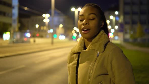 A Young Black Woman Talks to the Camera in a Street in an Urban Area at Night