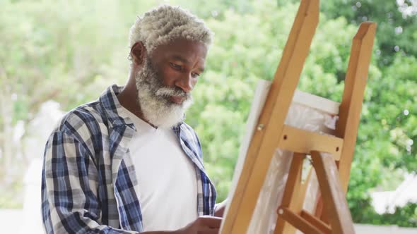 Video of african american senior man painting picture outside