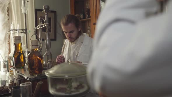 Young Concentrated Man Checking Medicines in Ancient Pharmacy. Guy Writing with Feather Pen When