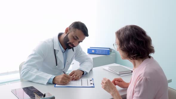 Smiling Indian Doctor Having Appointment with Female Patient in Hospital