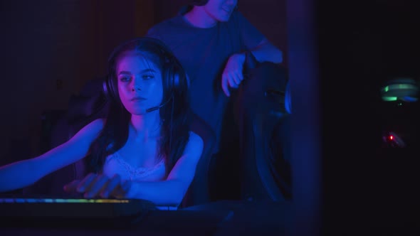 Two Girls Playing an Online Game in the Neon Gaming Club - Their Friend Comes To Them and Starts