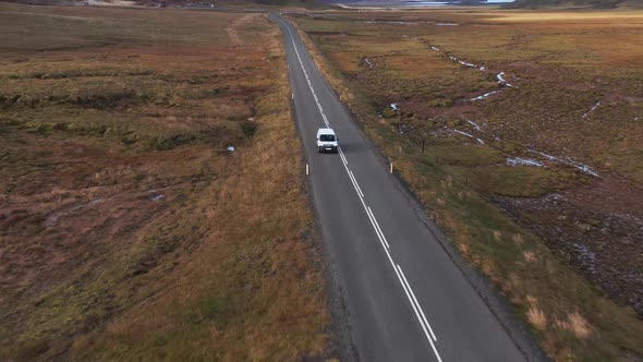 Car drives on long open road in tundra valley landscape, front aerial