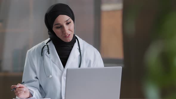 Arabian Female Therapist Doctor Wear Hijab White Coat Calling Distant Patient on Laptop Talking with