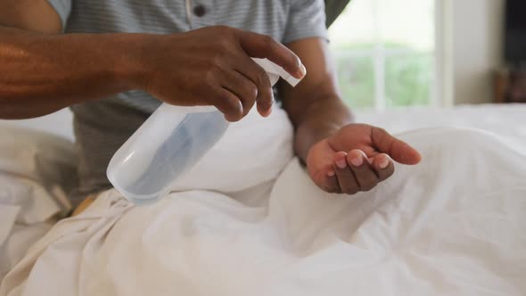 Mid section of african american senior man sanitizing his hands while sitting on the bed at home
