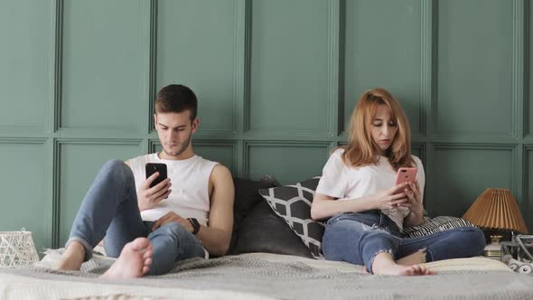 Young Couple Are Browsing Smartphones in Their Bed at Home