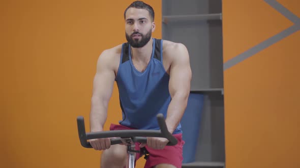 Portrait of Concentrated Muscular Middle Eastern Man Riding Exercise Bike in Gym. Confident Strong