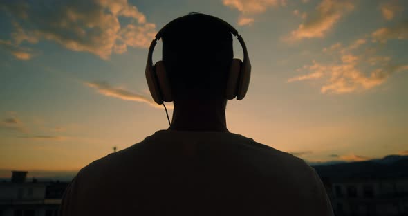 Boy listening to music outdoors while watching the sunset.