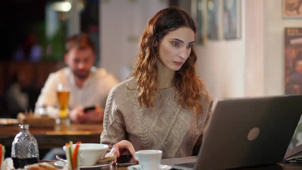 Woman Freelancer Works Outside the Home Female Developer Sits at the Bar and Works at a Laptop Uses