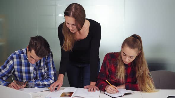 Three Students Working on Their Homework Sitting Together at the Table While One Girl is Dictating