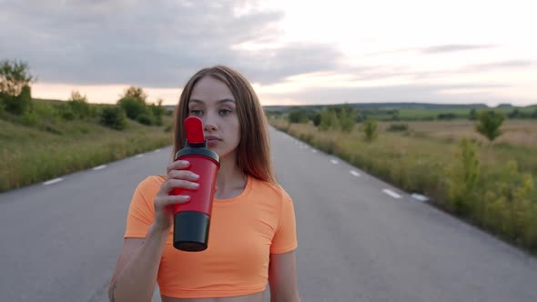 Purposeful Young Girl Stands on a Path and Drinks From Sport Flask in Morning