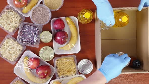 Top View, Close-up, Volunteers in Protective Gloves Pack Grocery To Cardboard Donation Box, Takeaway