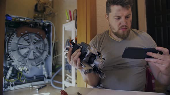 A Man Fixes a Washing Machine and Watches Instructions on His Phone