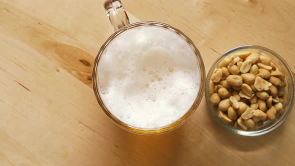 Top View of Beer with Foam and Salty Peanuts and on Wooden Table