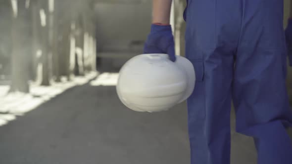 Close-up of White Helmet in Hands of Caucasian Man Walking on Building Site in Sunlight. Male