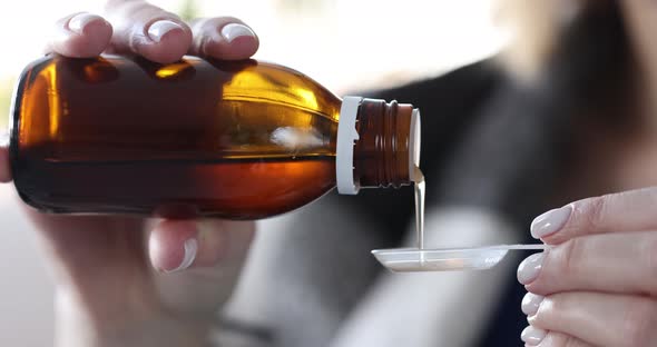 Person Pours Medicinal Syrup Into Spoon Closeup